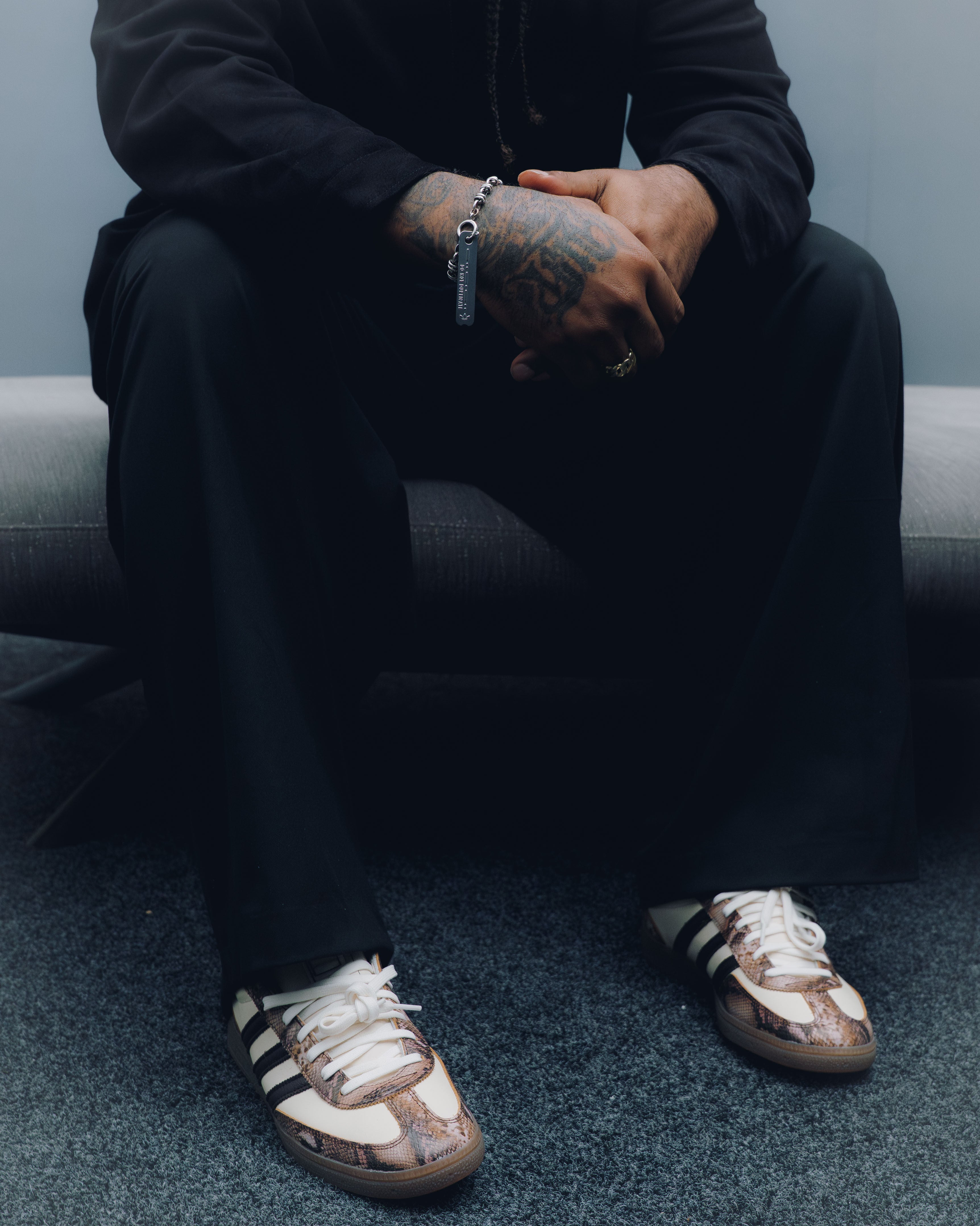Man in black streetwear pants sitting, wearing white and brown sneakers with black stripes