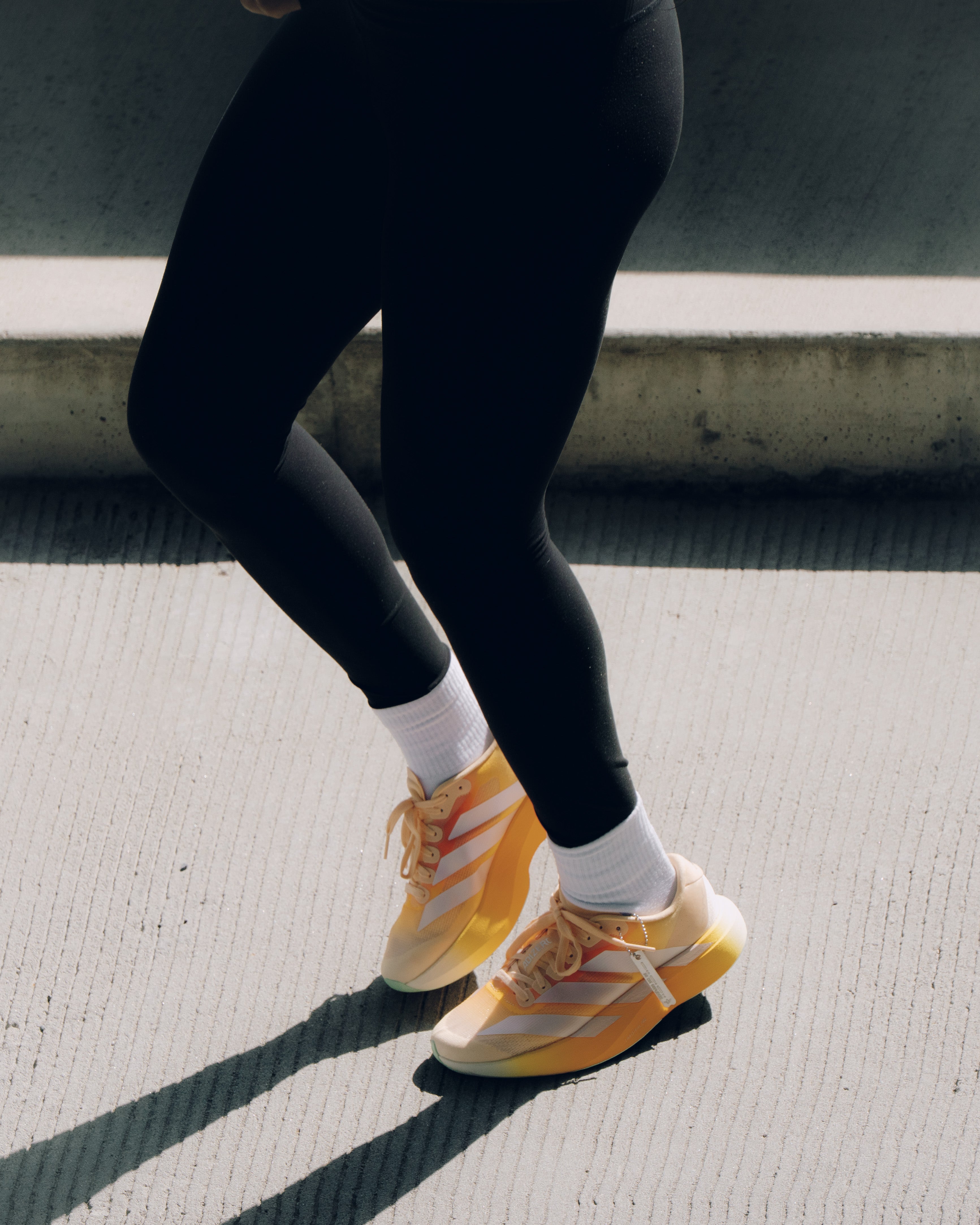 Person wearing black leggings and orange white sneakers on concrete steps, streetwear style