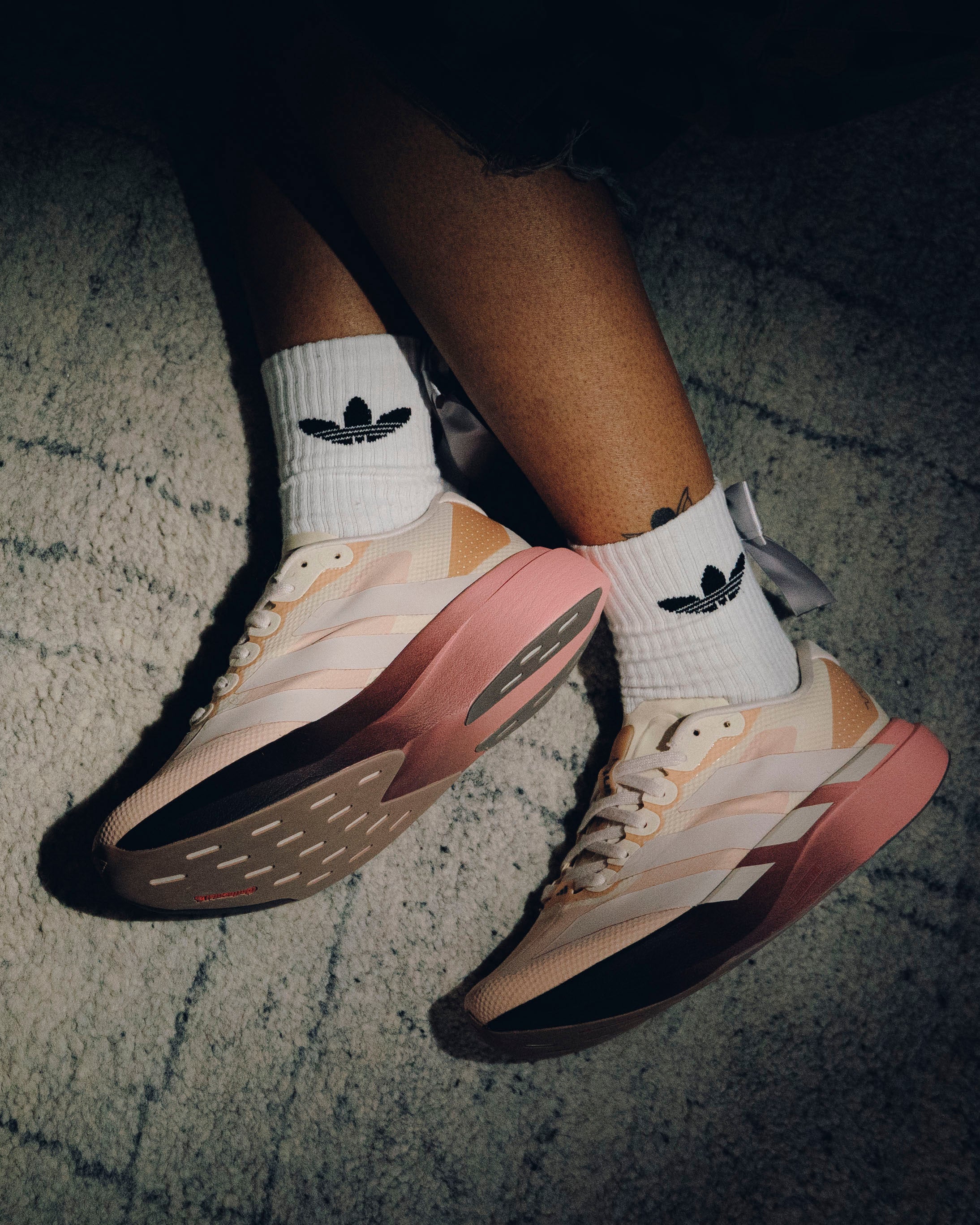 Pastel pink and beige Adidas sneakers with white striped socks on textured carpet