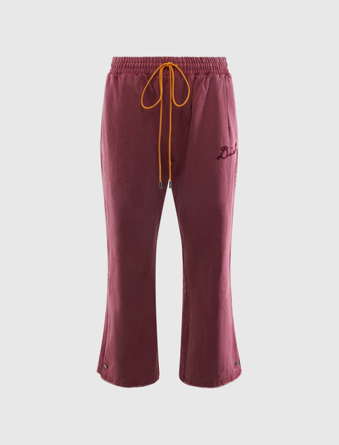 Burgundy velour track pants with yellow drawstring and embroidered script on left leg