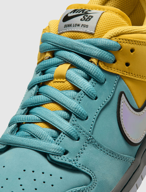 Close-up of Nike SB Dunk Low Pro sneaker with teal and yellow leather upper, blue laces, and iridescent Swoosh logo.