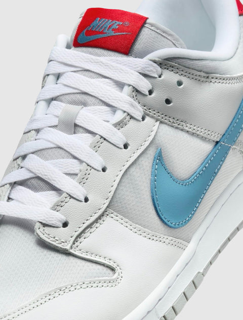 Close-up of white and grey sneaker with blue swoosh and red tongue label, white laces