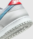 Close-up of Nike Dunk Low sneaker in light grey with blue swoosh and red heel tab