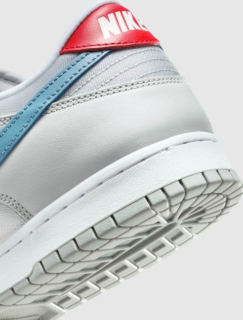 Close-up of Nike Dunk Low sneaker in light grey with blue swoosh and red heel tab