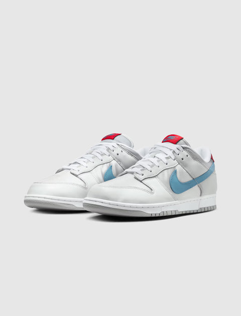 White and silver low-top sneakers with blue Swoosh and red tongue accents on a plain background