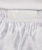 Close-up of white athletic shorts waistband with textured logo patch and subtle snake pattern