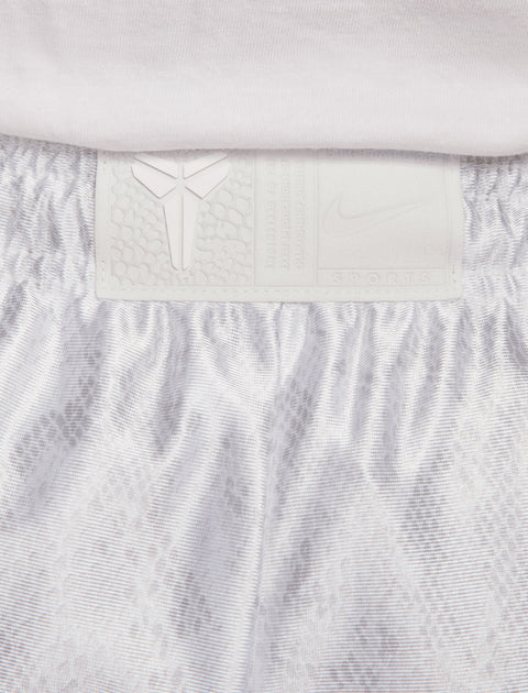 Close-up of white athletic shorts waistband with textured logo patch and subtle snake pattern
