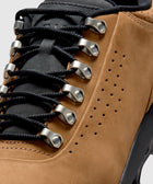 Close-up of taupe suede sneaker with black laces, metal eyelets, and perforated details