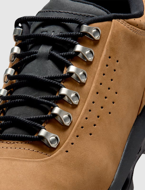 Close-up of taupe suede sneaker with black laces, metal eyelets, and perforated details