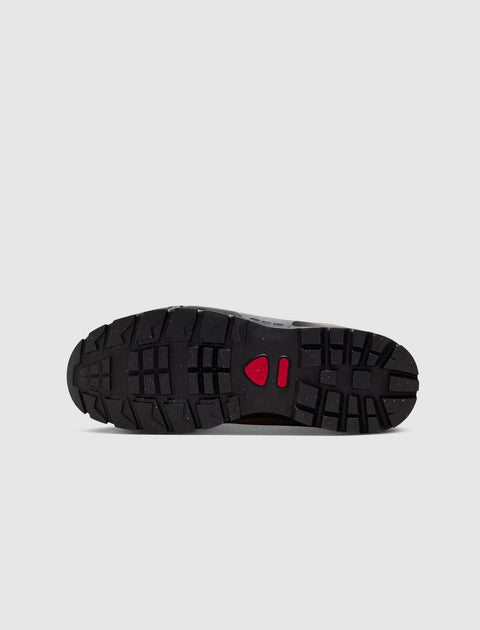 Black rubber sneaker sole with rugged tread and red accent on a light background
