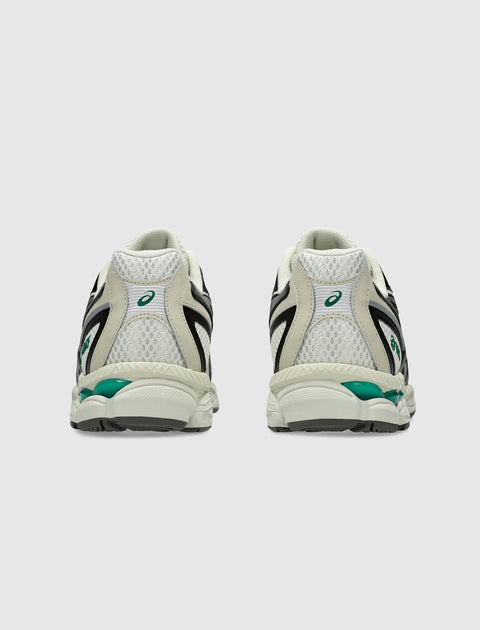 Rear view of beige mesh sneakers with black and green accents on a plain background