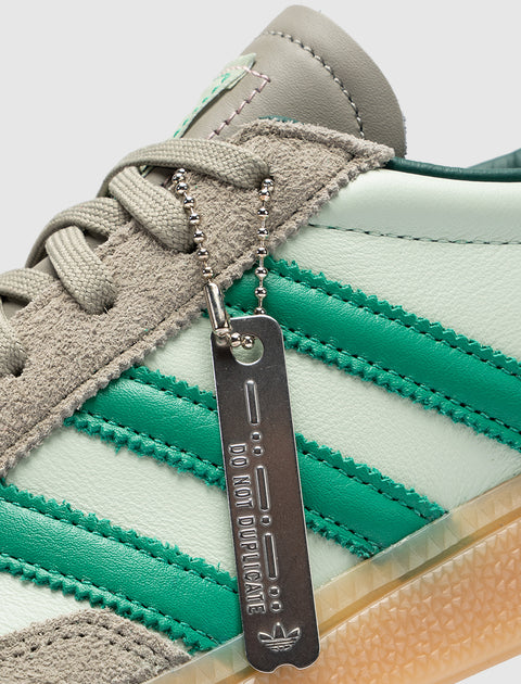 Close-up of mint green sneaker with suede trim, green stripes, and metal tag reading 'DO NOT DUPLICATE'.