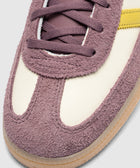 Close-up of mauve suede sneaker with cream panel, yellow stripe, and gum sole