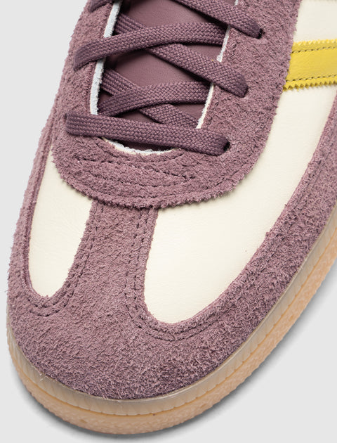 Close-up of mauve suede sneaker with cream panel, yellow stripe, and gum sole