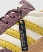 Close-up of sneaker with purple suede, yellow stripes, and metal tag reading 'DO NOT DUPLICATE'