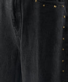 Close-up of black denim pants with gold stud embellishments on the pocket and seam