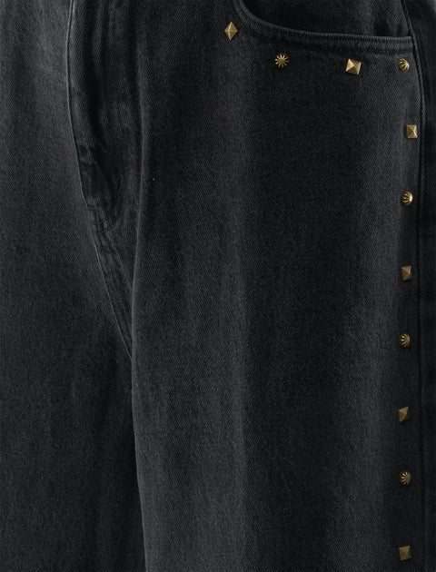 Close-up of black denim pants with gold stud embellishments on the pocket and seam