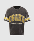 Black graphic streetwear t-shirt with yellow 'Osaka' print and varsity stripes on sleeves.