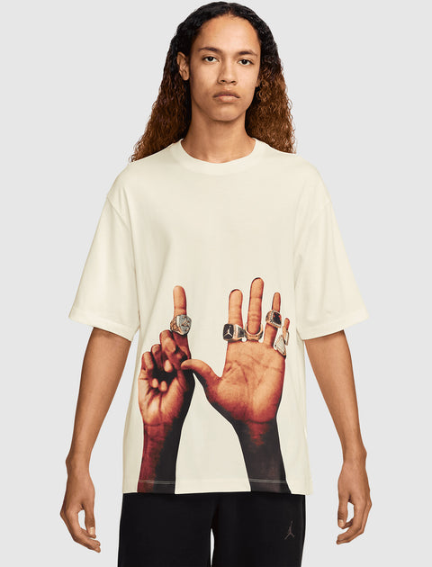 Man wearing cream streetwear t-shirt with graphic of hands displaying rings on the front