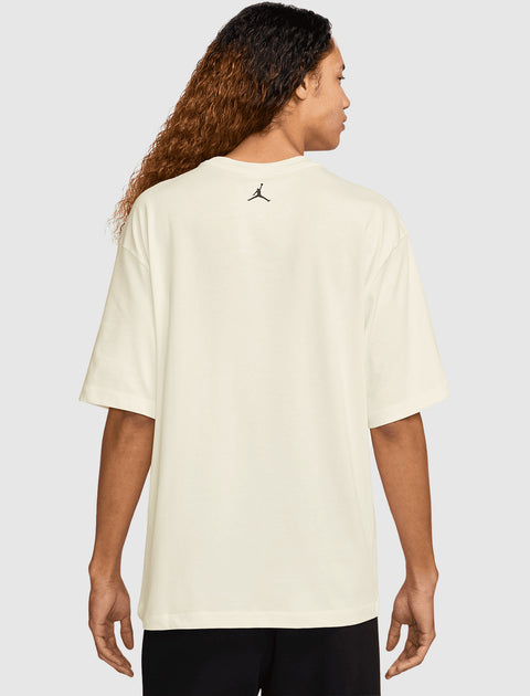 Man wearing an oversized cream t-shirt with small black logo on upper back, streetwear style