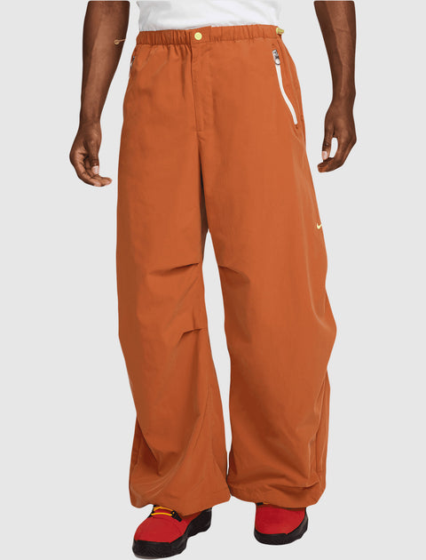 Man wearing loose orange streetwear pants with zip pockets and red sneakers