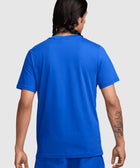 Man wearing a bright blue short sleeve t-shirt and shorts, shown from the back, tattoo visible on forearm