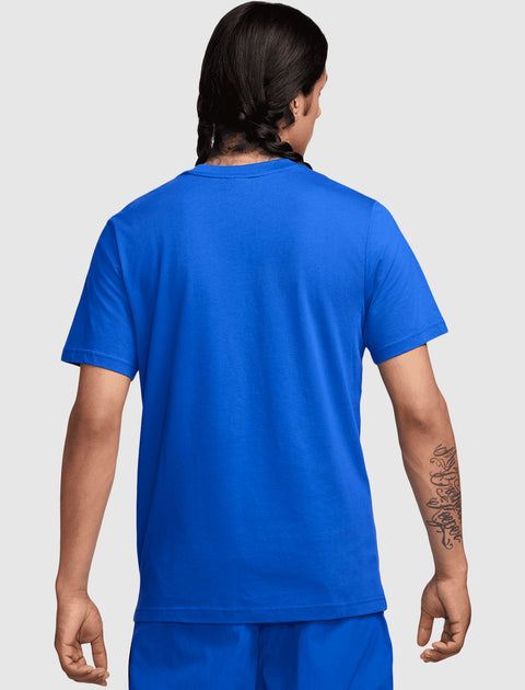 Man wearing a bright blue short sleeve t-shirt and shorts, shown from the back, tattoo visible on forearm
