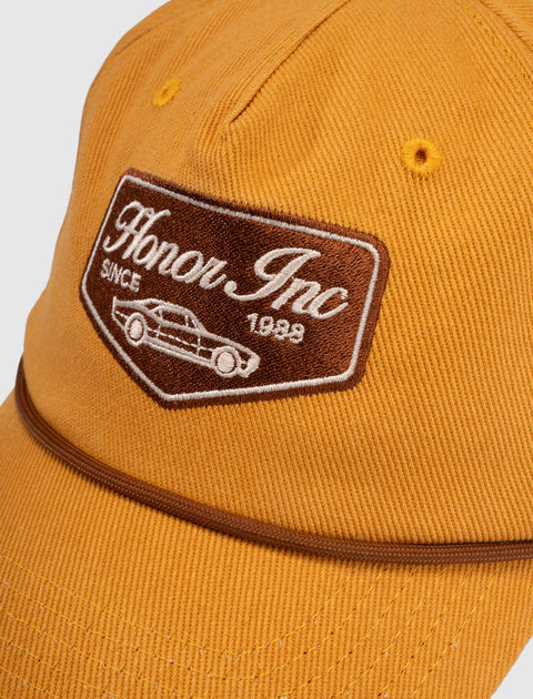 Yellow streetwear baseball cap with brown embroidered Honor Inc patch and car design