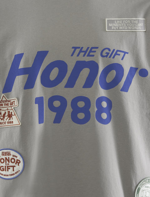 Gray streetwear t-shirt with bold blue 'Honor 1988' text, graphic patches, and slogan detail.
