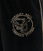 Close-up of black textured pants with beige piping and embroidered ceramics studio patch