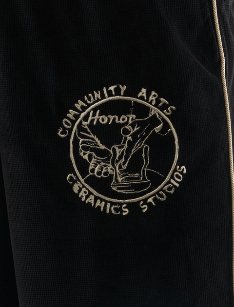 Close-up of black textured pants with beige piping and embroidered ceramics studio patch