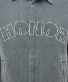 Closeup of light blue denim jacket with 'HONOR' embroidered in white on chest