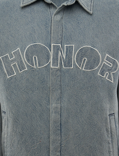 Closeup of light blue denim jacket with 'HONOR' embroidered in white on chest