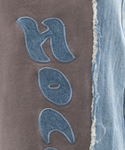 Close-up of grey streetwear fabric with blue denim applique lettering and raw denim edge