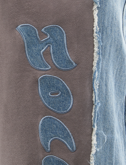 Close-up of grey streetwear fabric with blue denim applique lettering and raw denim edge