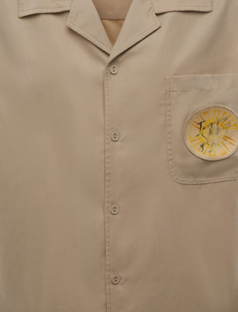 Beige button-up shirt with collar and sun graphic on front chest pocket