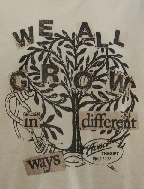 Cream streetwear tee with black graphic tree and 'We all grow in different ways' text print.