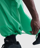 Close-up of hand adjusting green streetwear pants drawstring over black sneakers