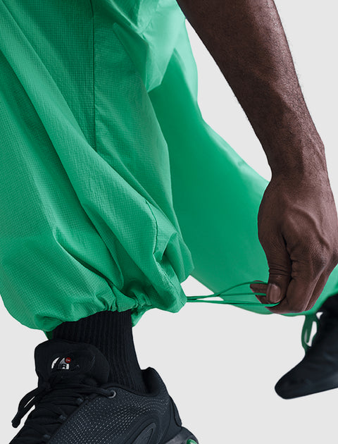Close-up of hand adjusting green streetwear pants drawstring over black sneakers