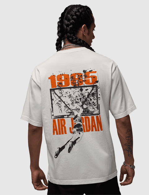 Back view of a man wearing a white Air Jordan 1985 graphic t-shirt, featuring a basketball dunk illustration.