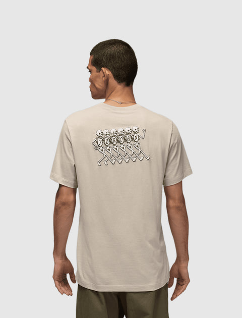 Back view of man in beige graphic streetwear t-shirt with cartoon skeletons print.