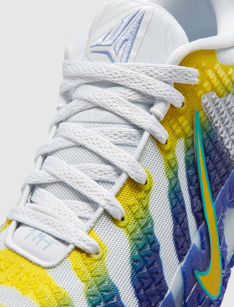 Close-up of white sneaker with blue, yellow, and green accents, mesh upper, and textured sole