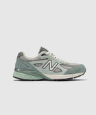Side view of grey and green suede mesh men's streetwear sneaker on white background