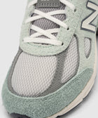Close-up of light green and grey suede mesh sneaker with 990v4 on tongue, lace-up detail