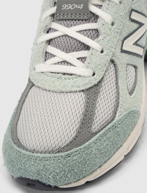 Close-up of light green and grey suede mesh sneaker with 990v4 on tongue, lace-up detail