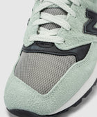 Close-up of mint green suede and grey mesh sneaker with white laces and black accents