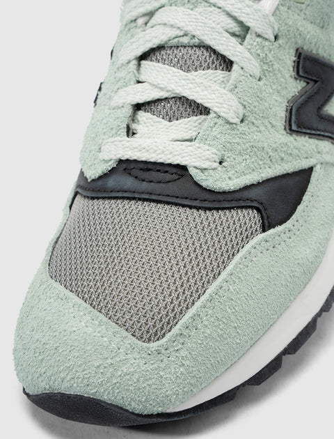 Close-up of mint green suede and grey mesh sneaker with white laces and black accents