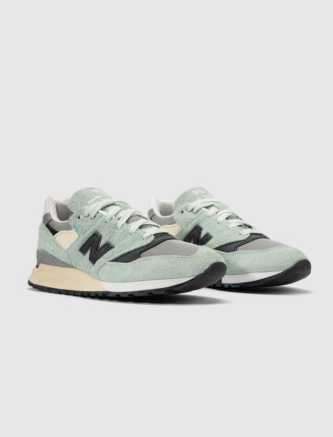 Mint green and black suede sneakers with beige accents on a white background