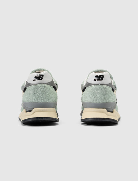 Rear view of pale green suede sneakers with white and black heel detail, casual footwear