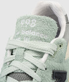 Close-up of mint green suede sneaker, textured tongue, woven laces, and side patch logo